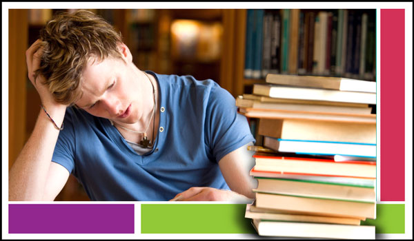 A boy studying and lots of books piled in front of him