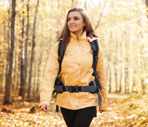 Smiling woman wearing yellow jacket walking in forest