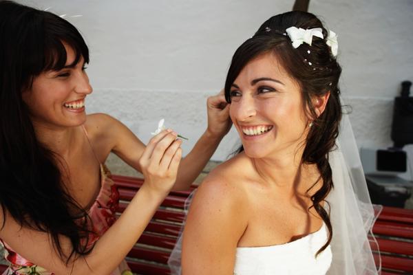 Young woman putting flower in bride's hair, smiling